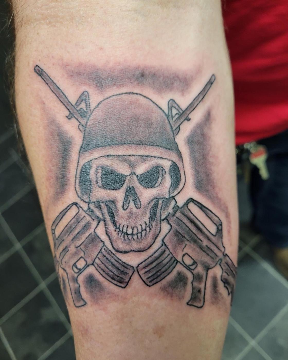 A black and gray skull with two crossed pistols behind it, on an arm